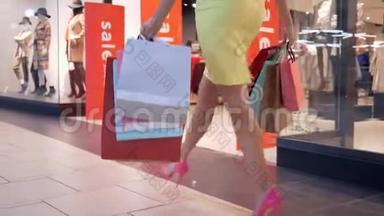 穿着时髦亮色鞋子、带购物袋的购物狂女孩的腿在打折、发短信的季节走在购物中心
